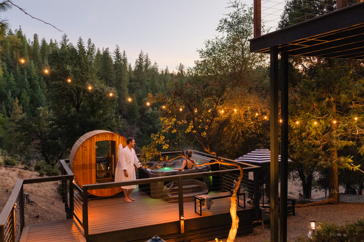 A couple at the hot tub at dusk, the sauna beside them